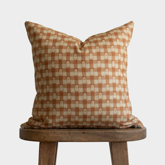 Rust and cream gingham pillow with small ghost motifs, displayed on wooden stool.