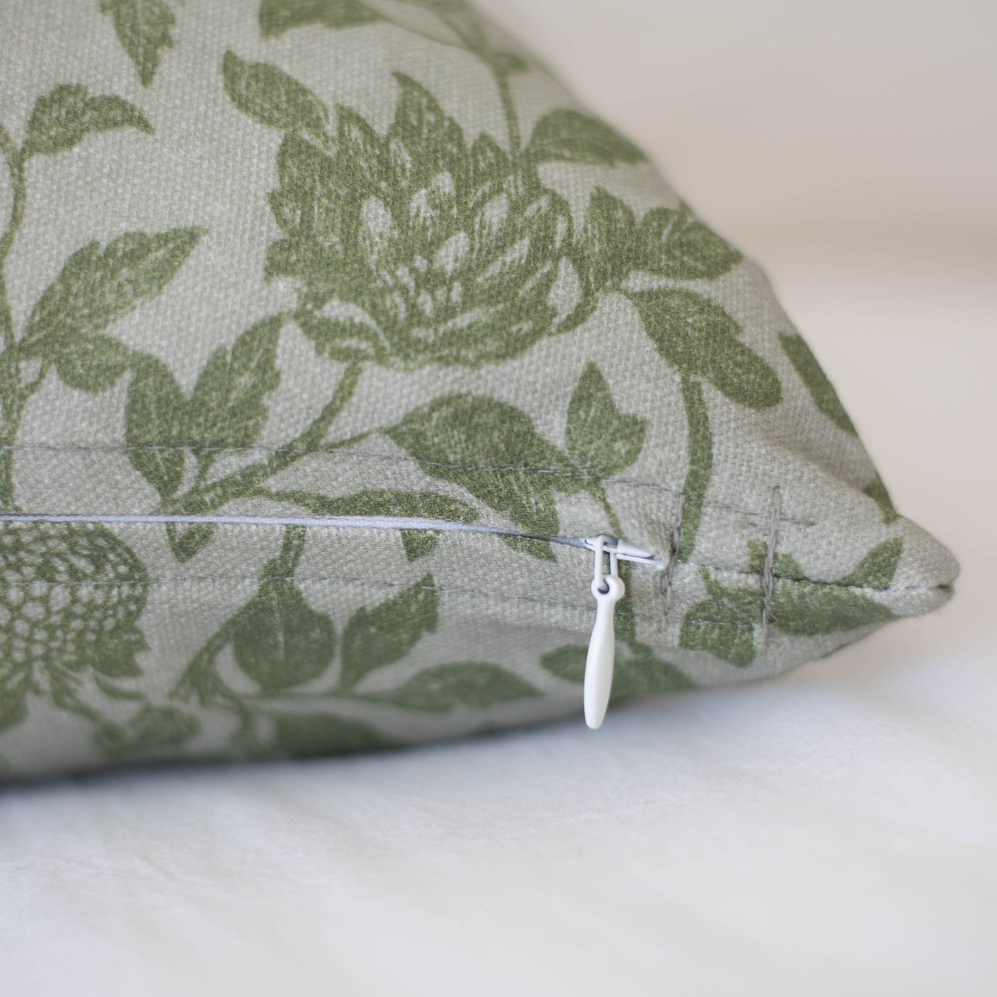 Cream-colored pillow cover with green ivy leaf pattern and white zipper closure visible on side.