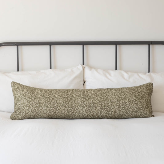 Long rectangular lumbar pillow with green and cream damask pattern on white bedding with black metal headboard.