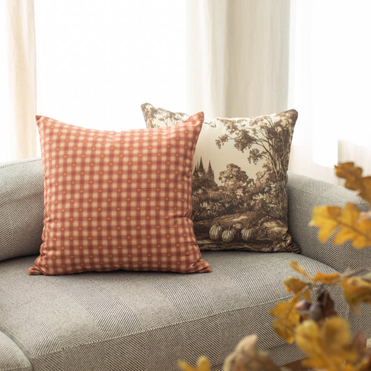 Orange and white gingham plaid pillow displayed on a gray geometric patterned blanket with autumn foliage nearby.