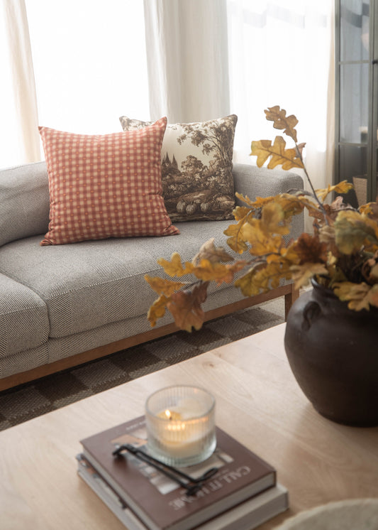 Orange and white gingham plaid throw pillow displayed on a gray sofa next to a toile pillowcase.