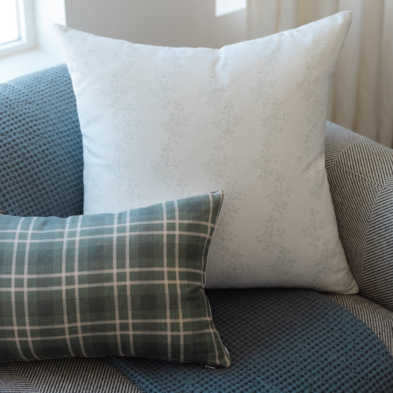 White throw pillow with subtle floral pattern displayed on a couch with blue and gray textured pillows.
