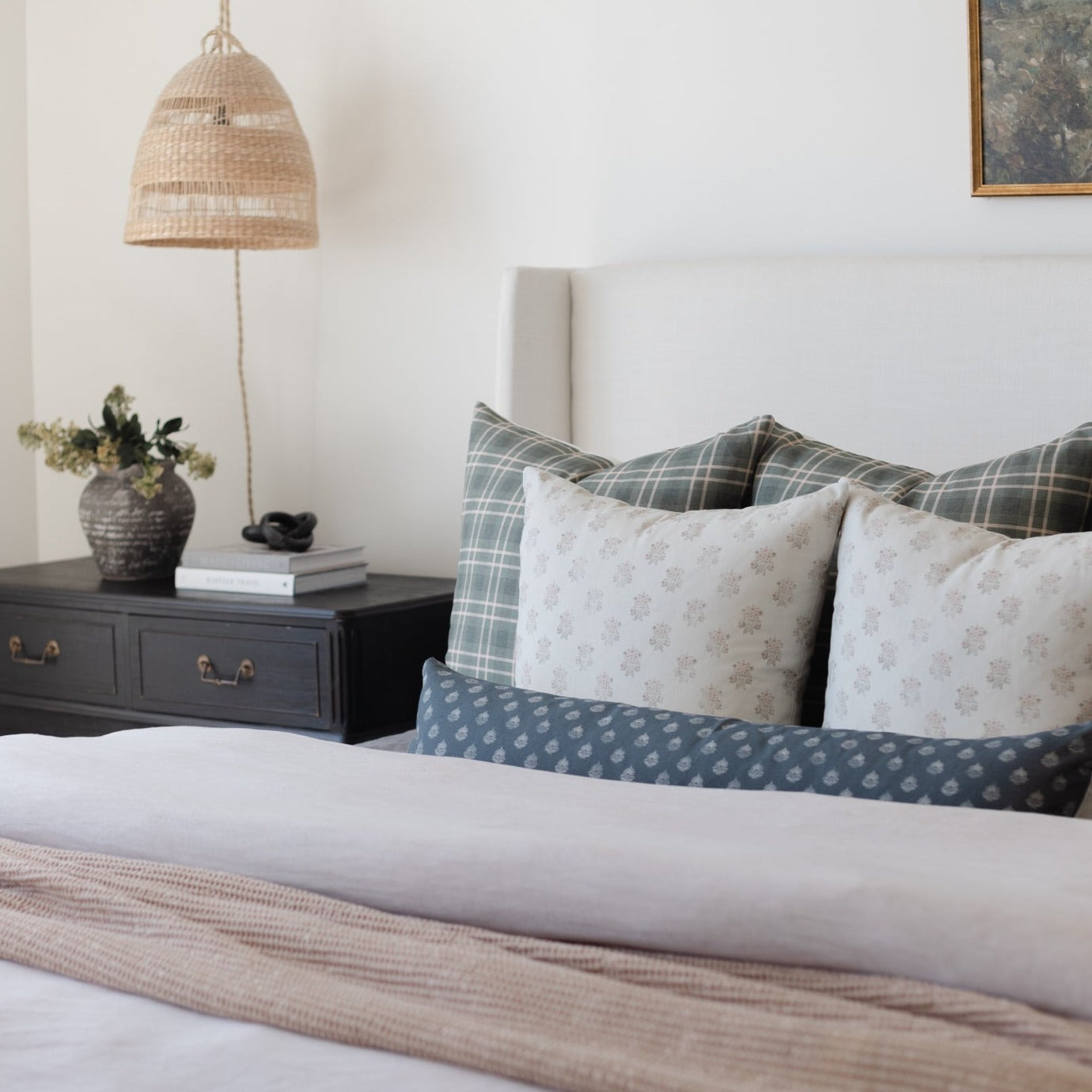 Blue lumbar pillow with vintage clay pattern displayed on bed with plaid and floral pillows.