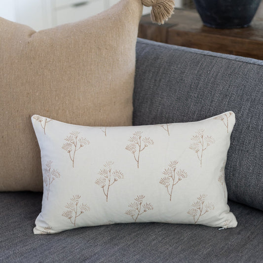 Cream lumbar pillow with tan thistle plant print, displayed on gray sofa with beige pillow.