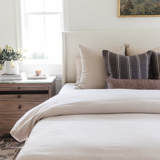 Tan and white gingham patterned pillow displayed on a bed with striped and solid throw pillows.
