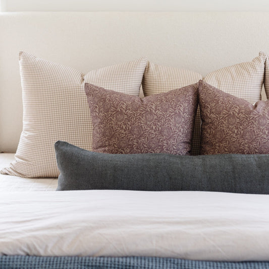 Tan and white gingham pillows arranged on a bed with patterned and solid accent pillows.