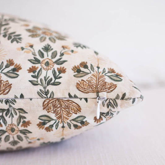 Cream pillow with embroidered botanical pattern in brown, tan, and green featuring flowers and leafy stems with zipper closur