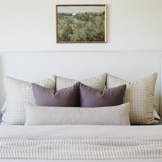 Tan lumbar pillow with vertical striped pattern displayed on bed between checkered accent pillows.