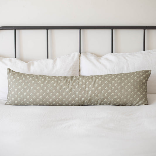 Sage green lumbar pillow with small white floral pattern on bed with white pillows and metal headboard.