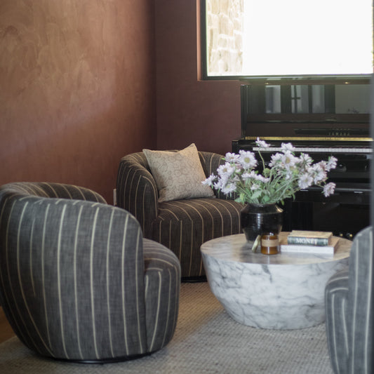 Beige linen pillow cover with subtle floral pattern, displayed on striped chair in modern living room setting.