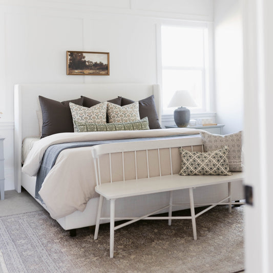 Green and cream floral patterned linen pillow displayed on a bed with black and neutral bedding.