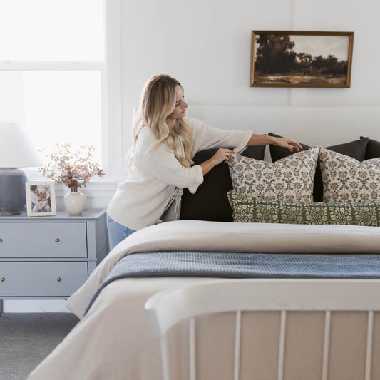 Rectangular lumbar pillow with green and cream floral pattern displayed on a bed with black headboard and bedding.