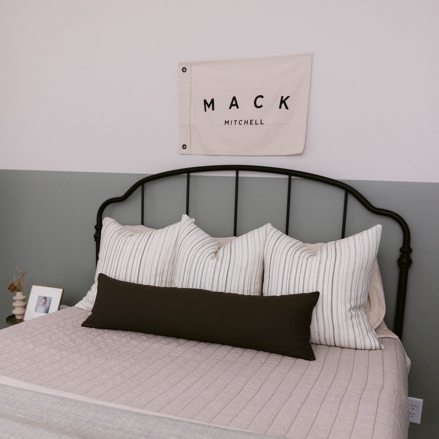 Black double-sided lumbar pillow on bed with striped pillows and quilted bedding.