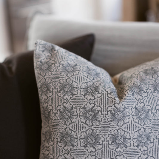 Cream and gray throw pillow with floral damask pattern displayed on a gray sofa.