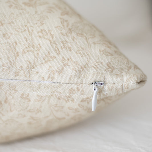 Beige decorative pillow with damask pattern and white zipper closure.