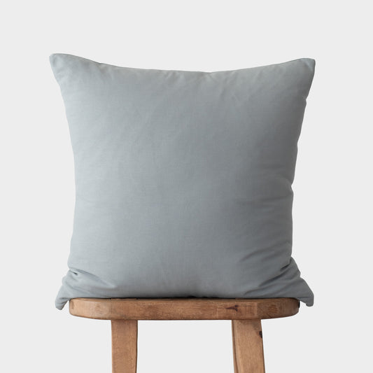 Light blue square throw pillow displayed on a wooden stool against a neutral background.
