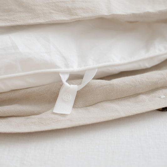 Beige and cream folded duvet cover with white button closure tab visible on layered fabric.