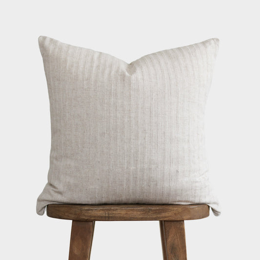 Cream textured pillow with vertical ribbed pattern resting on wooden stool.
