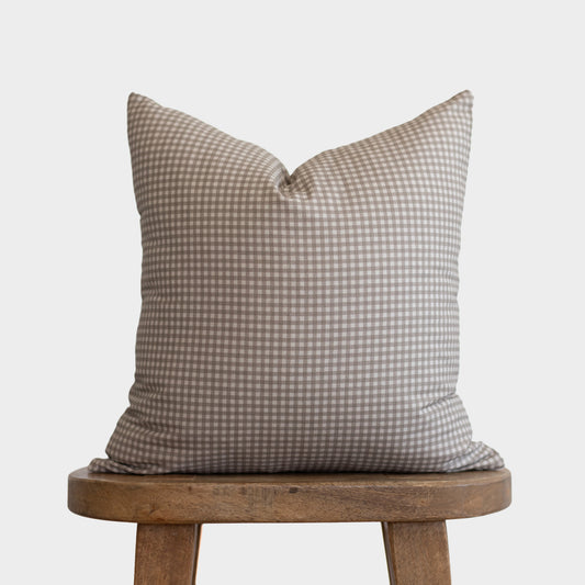 Tan and white gingham patterned pillow with small checks resting on wooden stool.