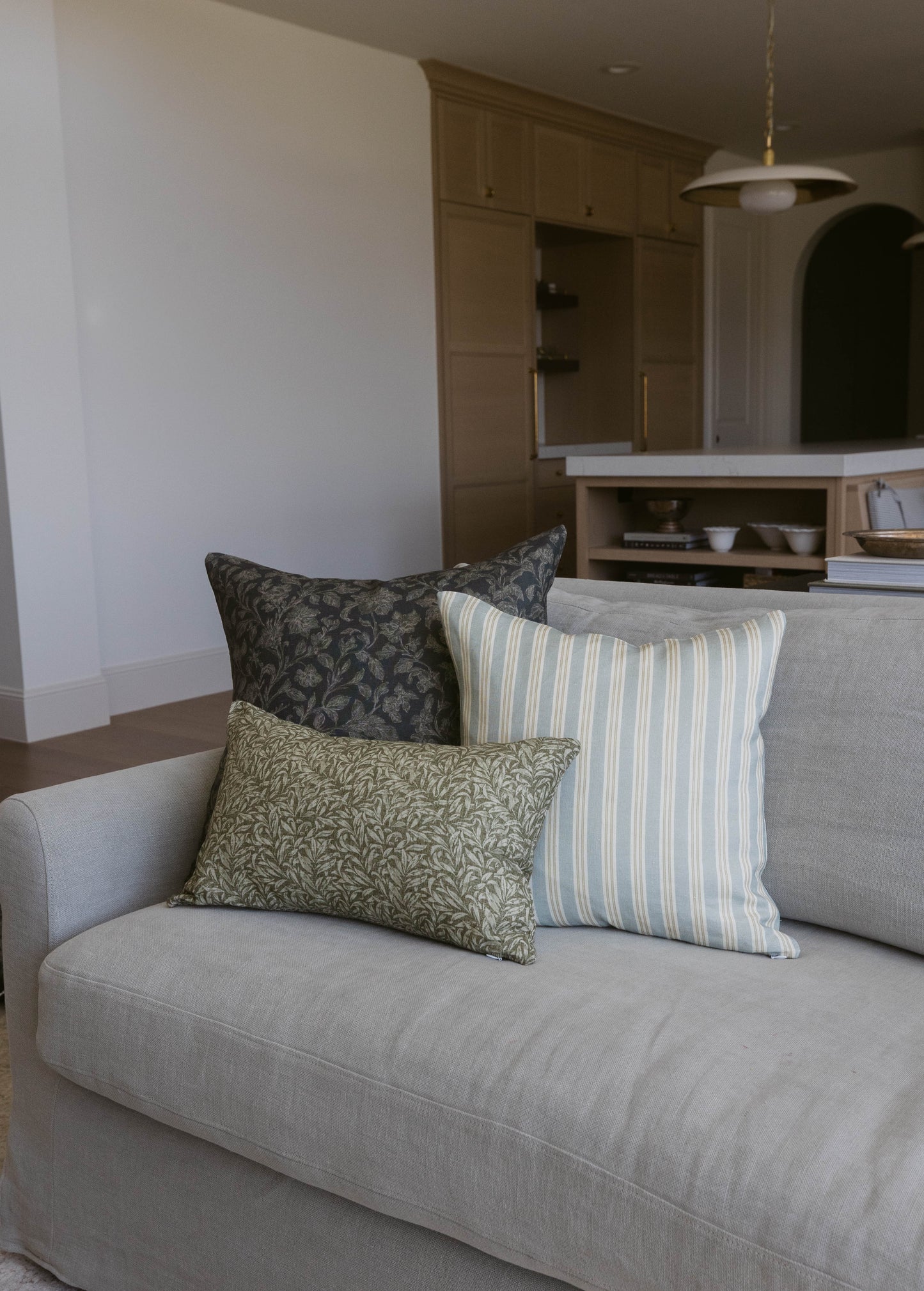Three decorative pillows with leaf and stripe patterns arranged on a gray upholstered sofa.