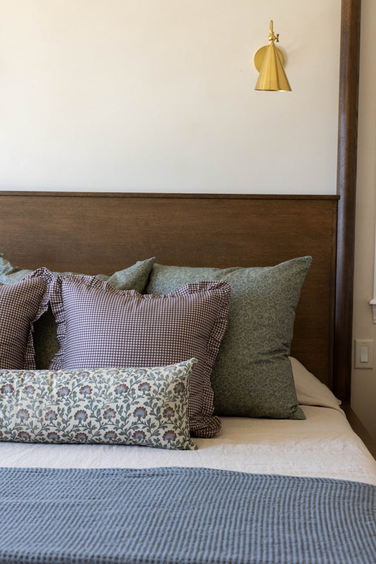 Plum and white mini gingham pillow with ruffled edges displayed on a bed with coordinating decorative pillows.
