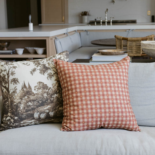 Pumpkin-colored gingham plaid pillow displayed on a light gray sofa next to a toile-patterned pillow.