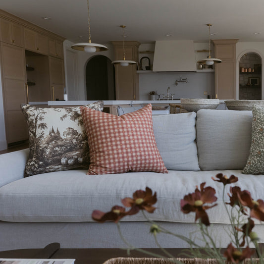 Orange and white gingham plaid throw pillow displayed on a gray sofa with coordinating pillows.