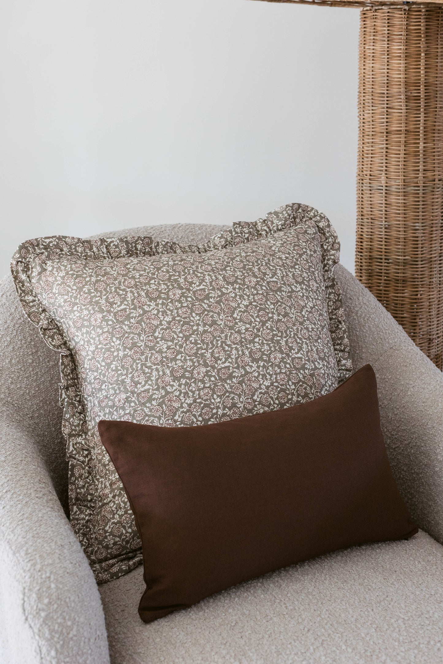 Beige patterned pillow with ruffled edges and brown solid pillow on light gray chair with wicker basket.