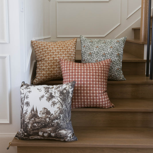 Four decorative pillows with various patterns displayed on wooden stairs: tan checkered, red gingham, gray floral, and gray s
