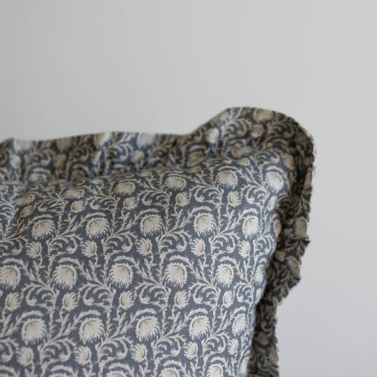 Blue and cream damask patterned pillow with ruffled edges and scrolling floral design.
