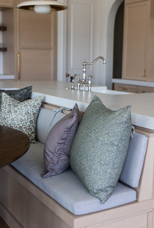 Green and plum patterned pillows with ruffle edges arranged on bathroom counter.