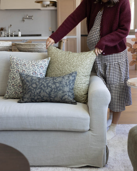 Three patterned throw pillows in green, blue, and neutral tones arranged on a cream-colored sofa.