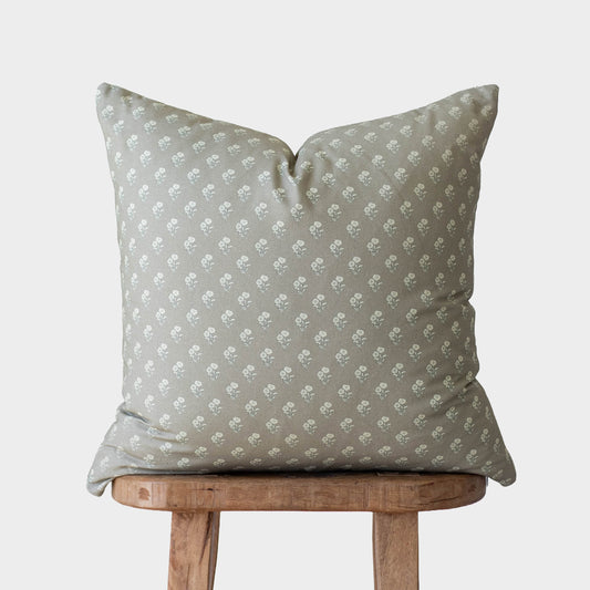 Sage green pillow with small white floral pattern, displayed on wooden stool.