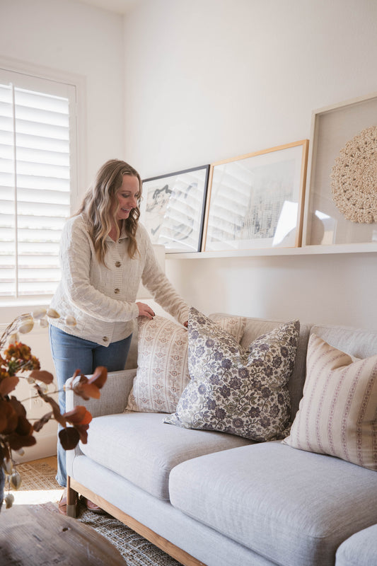 Light gray upholstered sofa with wooden frame, styled with patterned throw pillows in neutral tones.