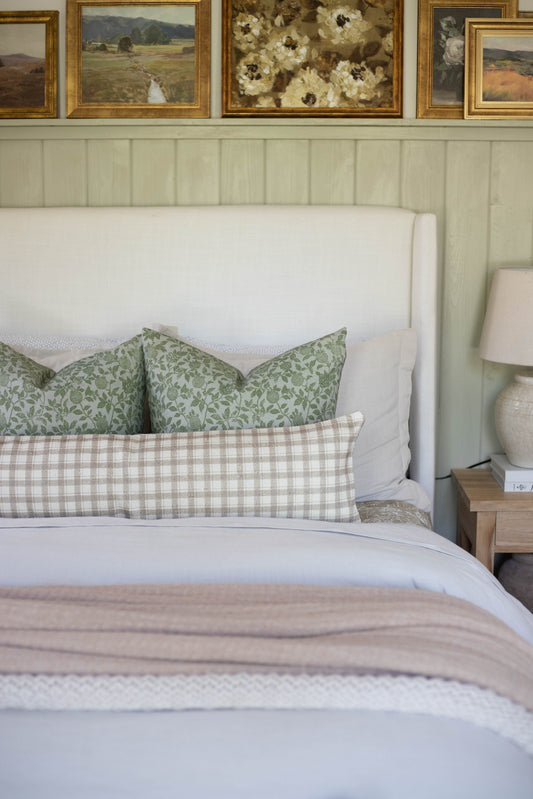 Beige and white gingham cotton lumbar pillow on bed with green patterned pillows and white headboard.