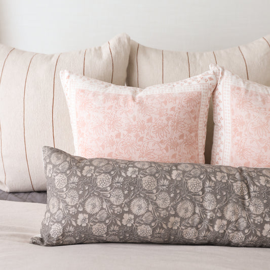Gray lumbar pillow with white floral botanical print, displayed with pink and cream striped pillows on a bed.