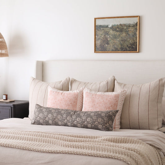 Rectangular lumbar pillow with gray floral pattern displayed on bed with pink and striped pillows.