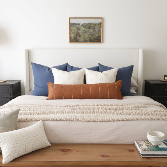 Navy blue and cream decorative pillows arranged on a bed with a rust-colored striped lumbar pillow in the center.