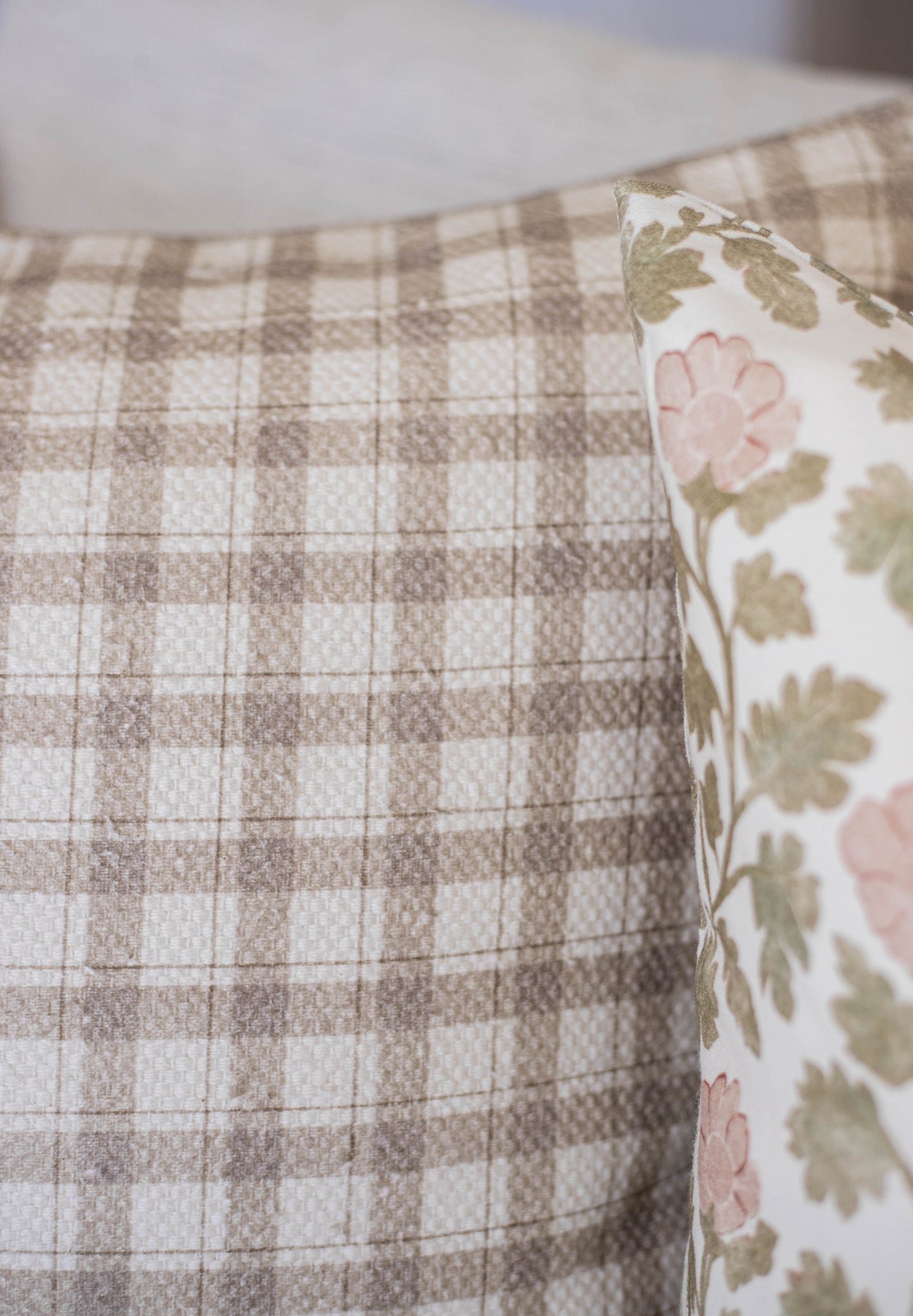 Beige and white checked cotton fabric with a floral patterned pillow showing pink flowers and green leaves.