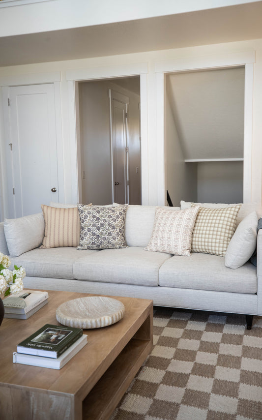 Four decorative throw pillows in neutral tones with striped, floral, solid, and checkered patterns displayed on a light gray