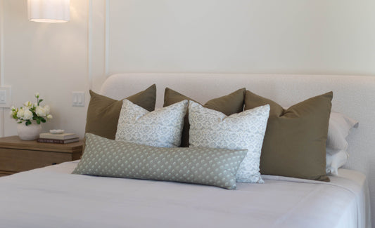King bed with five pillow covers in olive green and light blue patterned designs arranged against headboard.