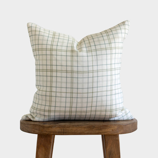 Beige and gray plaid linen pillow on wooden stool against white background.