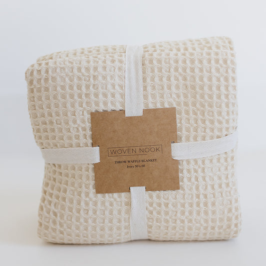 Ivory waffle blanket with textured grid pattern, rolled and wrapped with cream cotton band and kraft paper label.