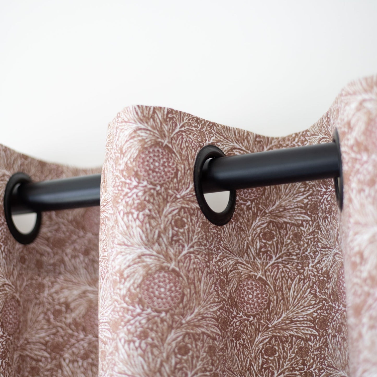 Pair of mauve curtain panels with botanical print pattern hung on black rod with grommet top rings.