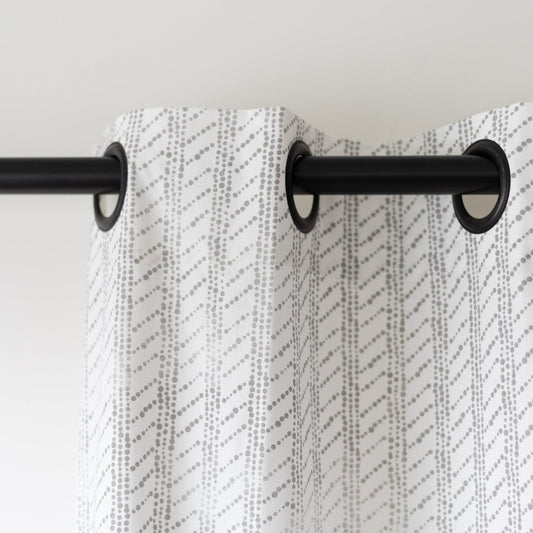 Two white curtain panels with gray diagonal dot pattern hanging from black grommet rings on a rod.
