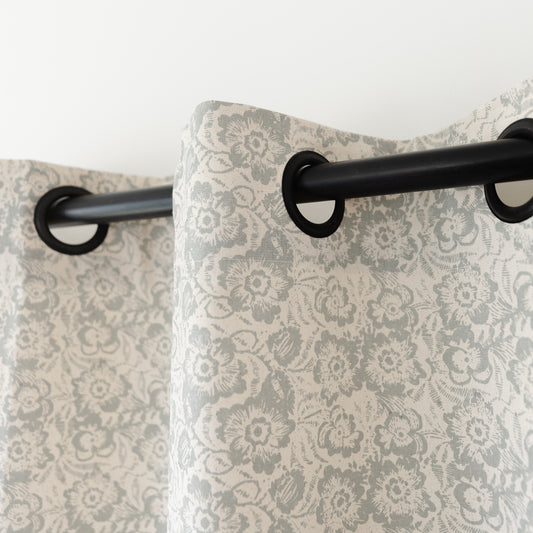 Two cream curtains with gray damask floral pattern hanging from black grommet rod.