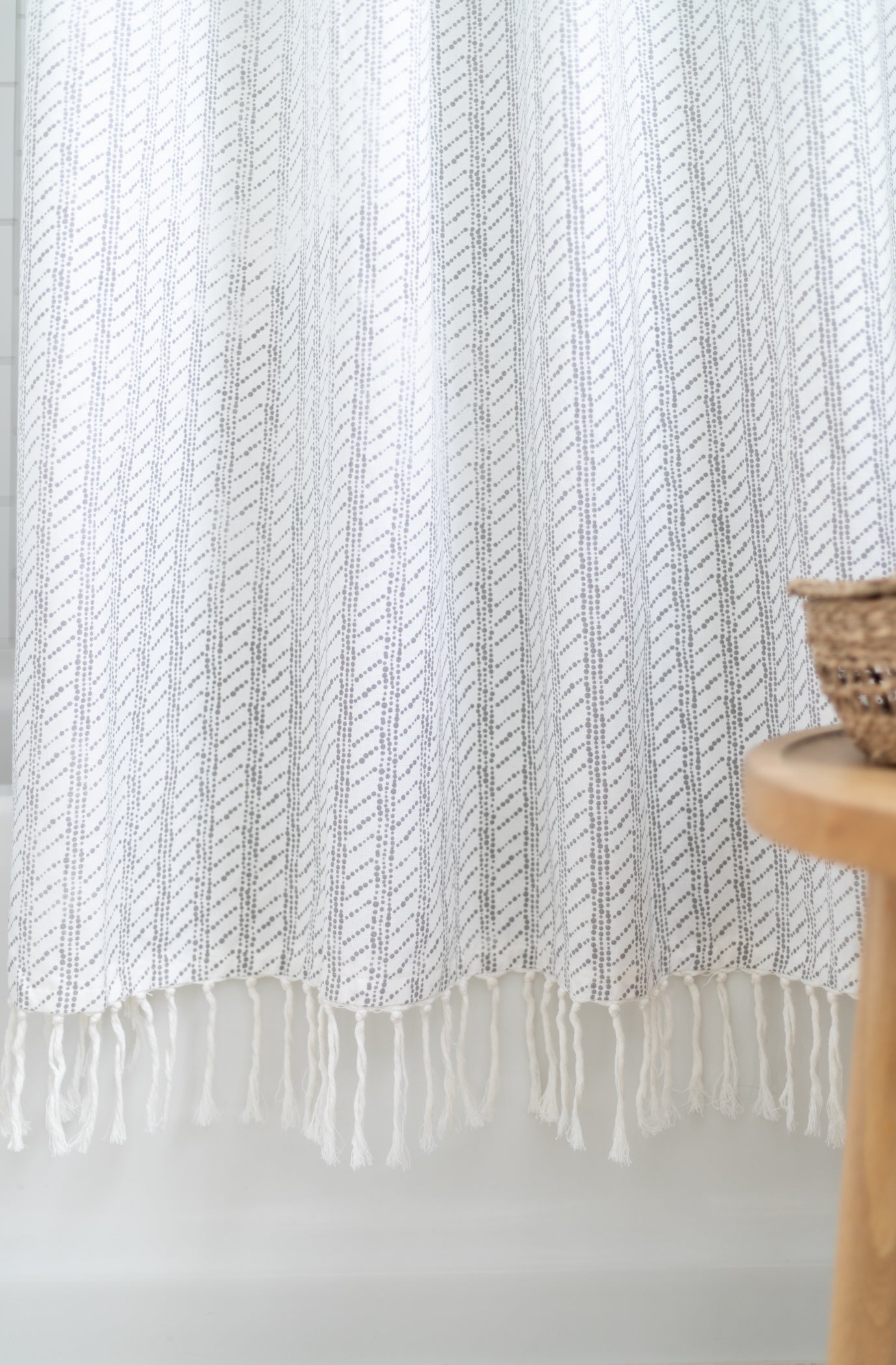 White shower curtain with gray diagonal stripe pattern and fringe trim at bottom edge.