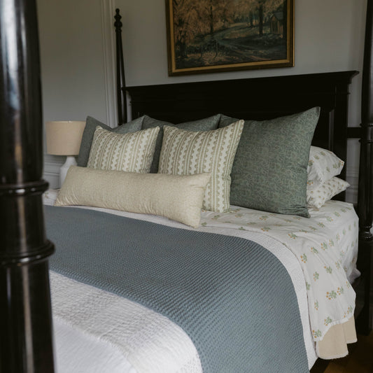 Arlo linen pillow in cream and sage green geometric patterns displayed on a black bedroom bed with matching bedding.