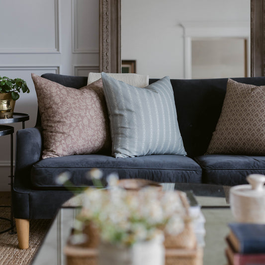 Four throw pillows in rose, light blue striped, black, and beige patterned fabrics arranged on a dark navy sofa.