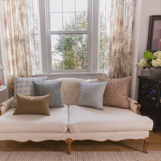 Cream upholstered sofa with wooden legs styled with patterned throw pillows in a living room setting.